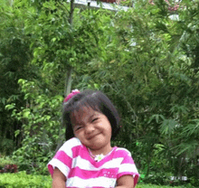 a little girl wearing a pink and white striped shirt is smiling for the camera .