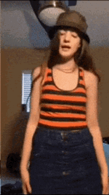 a girl wearing a striped tank top and a hat is standing in a room