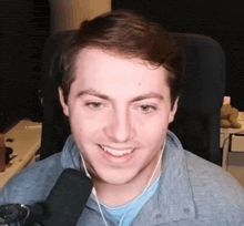 a young man is smiling in front of a microphone while wearing ear buds .