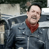 a man wearing a leather jacket and a scarf is standing in front of a car .