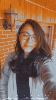 a woman wearing glasses is taking a selfie in front of a brick building