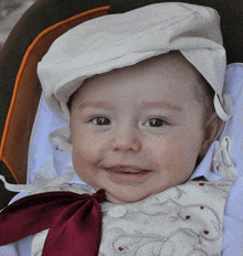 a baby wearing a white hat and a red bow tie smiles