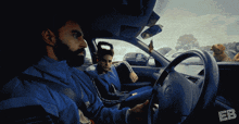 a man in a blue jacket is driving a car with a dog in the back seat