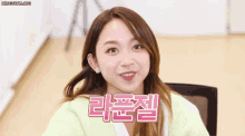 a woman in a green sweater is smiling in front of a sign that says ' korean ' on it