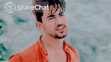 a man with a beard wearing an orange shirt is smiling in front of a sharechat logo .