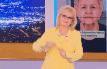 a woman wearing glasses and a yellow jacket is standing in front of a screen with a picture of a woman and the date 15 april