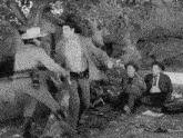 a group of men are having a picnic under a tree and one of them is holding a gun