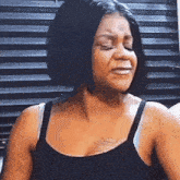 a woman in a black tank top is crying while standing in front of a window .