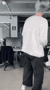 a man in a white shirt and black pants is standing in a room with a computer monitor .