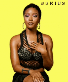a woman in a black top is sitting in front of a yellow background with the word genius written on it