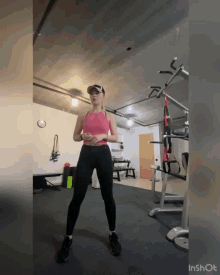 a woman in a pink tank top and black leggings is in a gym