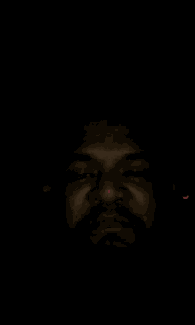a man with a beard is making a funny face in the dark with a red light behind him .