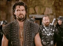 a man with a beard is standing in front of a group of men wearing leather armor .