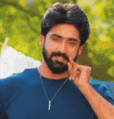 a man with a beard is wearing a blue shirt and necklace
