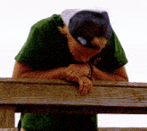 a man wearing a green shirt with jm on it leans over a wooden railing