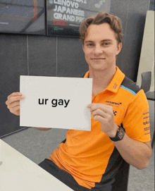 a man in an orange shirt is holding a sign that says ur gay