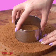 a person is cutting a cake with a stainless steel ring that says yum on the bottom right