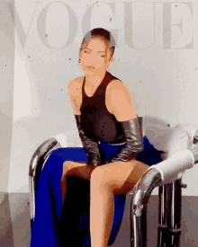a woman is sitting on a chair in front of a wall that has the word vogue on it