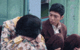 a man in a brown suit sits next to a woman with her head down