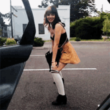 a woman in a yellow skirt and white knee high socks stands in a parking lot