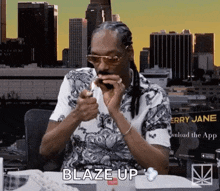 snoop dogg is sitting at a table with a lighter in his mouth and says blaze up