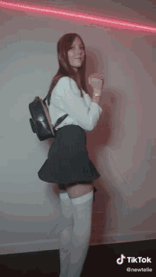 a woman wearing white thigh high socks and a black pleated skirt has a tiktok sticker on her shoulder