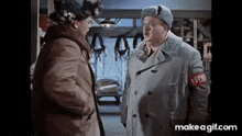 two men in coats and hats are standing next to each other in a room and talking .