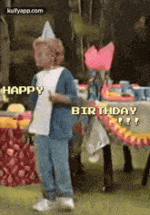 a little boy wearing a party hat is standing in front of a table with the words happy birthday written on it .