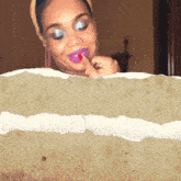 a woman with purple lipstick and blue eyeshadow holds her finger to her lips