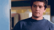 a man in a blue shirt is standing in front of a door looking at the camera .
