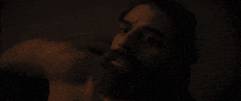 a man with a beard is laying down in the dark and looking up at the camera .