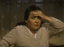 a woman holds her hand to her forehead while wearing a grey sweater