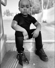 a young boy sits on a set of stairs wearing a black t-shirt and black pants