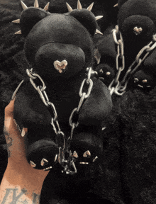 a person holding a black teddy bear with spikes and chains