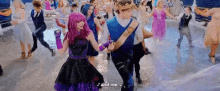a group of people are dancing in a crowd and one of them is wearing a purple dress .
