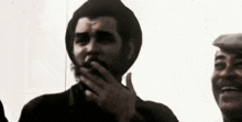 a man with a beard is covering his mouth with his hand while another man laughs .