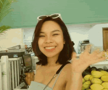 a woman wearing sunglasses smiles and waves her hand