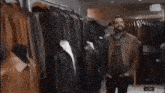 a man in a leather jacket is standing in front of a rack of clothes with 2:30 on the clock
