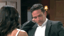 a man in a suit and white shirt is talking to a woman in a white tank top