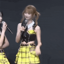 a woman in a yellow plaid skirt is holding a microphone and dancing .