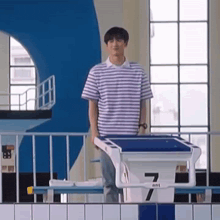 a young man in a striped shirt is standing on a diving board in a swimming pool .