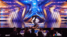 a man is doing a trick on a stage with a star in the background while a crowd watches .
