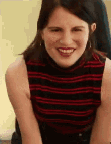 a woman in a red and black striped shirt is smiling and looking at the camera .