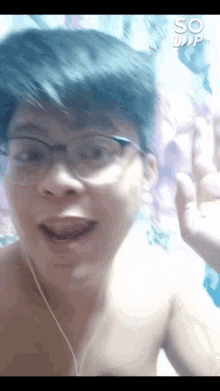 a shirtless man wearing glasses and ear buds waves his hand