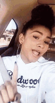 a woman is taking a selfie in the back seat of a car while wearing a white hoodie and earrings .