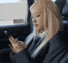 a woman in a suit sits in the back seat of a car looking at her cell phone