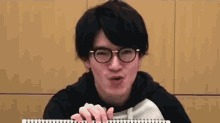 a young man wearing glasses is laughing and holding a notebook .