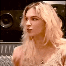 a woman with blonde hair and a necklace is standing in front of a mixer .