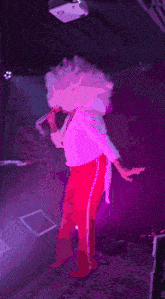 a person in a pink wig and red pants is holding a microphone