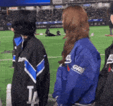 a woman wearing a dodgers jacket is standing on a baseball field with other people .